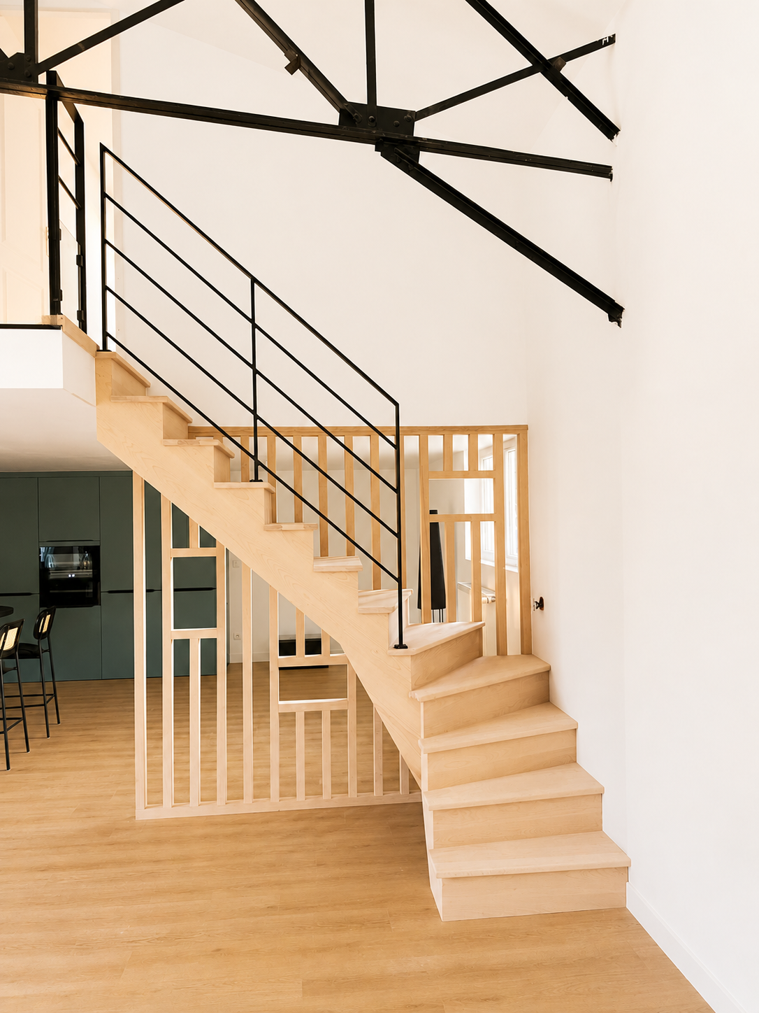 Escalier droit en bois clair avec garde-corps métal noir ouvert sur la cuisine