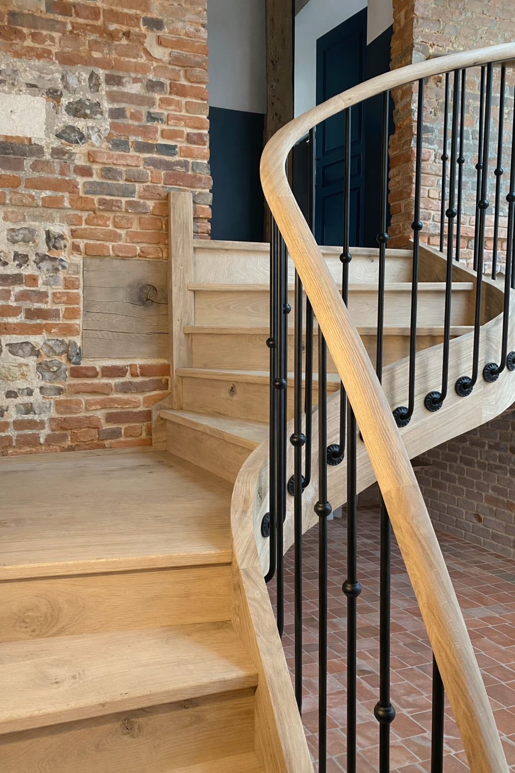 Escalier en bois clair et garde-corps fer forgé contre un mur de brique